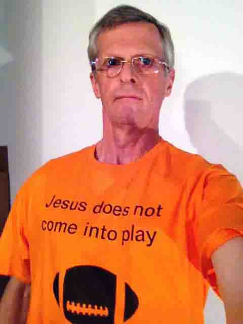 Darwin Bedford wearing his shirt that says 'Jesus does not come into play' and shows a football